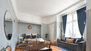 Un coin repas comprenant une table ronde, des chaises et un canapé, dans une pièce dotée d’une grande fenêtre et de rideaux.
