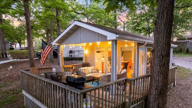 A small cabin with a deck, a covered porch, and a flag.