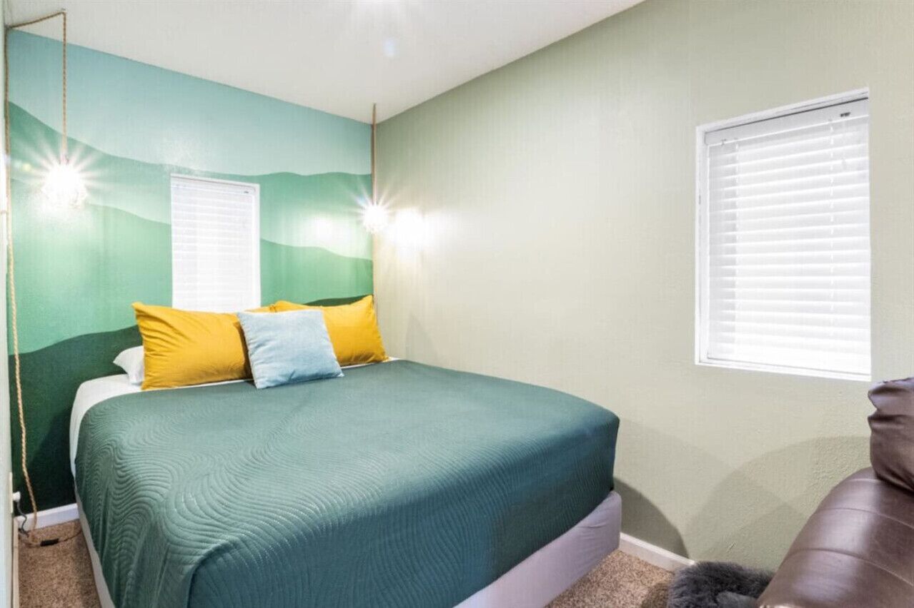 A bedroom with a bed, two bedside lamps, a window with blinds, and a brown leather chair.