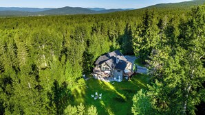 Una casa grande rodeada de un bosque frondoso, con una terraza amplia y zona de estar al aire libre.