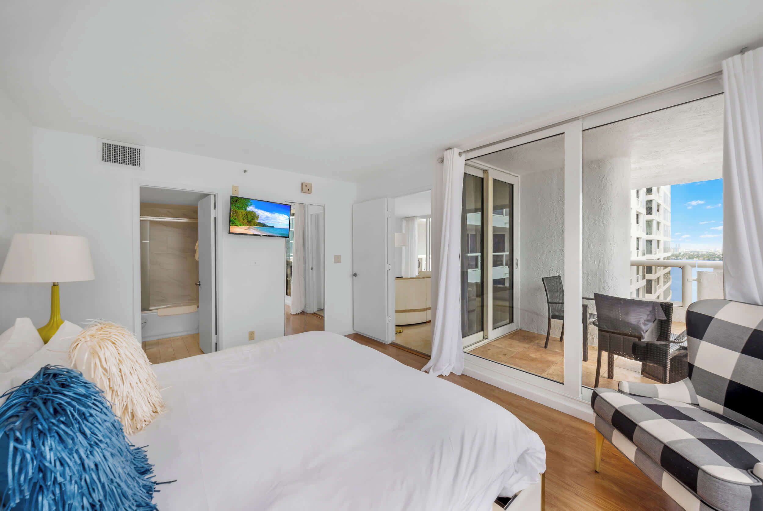 A hotel room with a bed, a TV, a balcony with a view, and a checkered sofa.