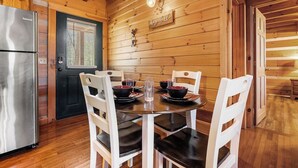 Interior de una cabaña de madera con una mesa de comedor preparada para cuatro personas, rodeada de sillas blancas.