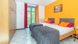 Une chambre avec deux lits, une armoire, une fenêtre avec des rideaux et un tableau au mur.