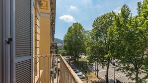 Un balcon doté d’une rambarde en métal, donnant sur une rue bordée de voitures garées et d’arbres.