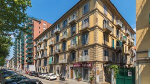 Un immeuble à plusieurs étages doté de balcons, avec une devanture visible et des voitures garées le long de la rue.