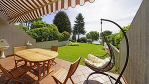 A patio with a wooden table and chairs, a hanging chair, and a view of a well-maintained lawn and trees. - Il Melagrano A6 by Wonderful Italy (Padenghe sul Garda)