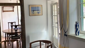 A room with exposed wooden beams, a dining table with chairs, a framed picture on the wall, a window with a curtain, and a vase on the windowsill. - Charmantes Renoviertes Haus in Altem Anwesen mit Privatem Innenhof und Parkplatz (Moigny-sur-Ecole)