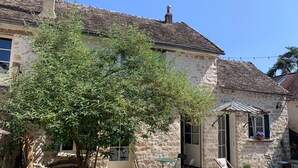 A stone building with a tiled roof, a small garden with a tree, outdoor seating, and a door leading to the interior. - Charmantes Renoviertes Haus in Altem Anwesen mit Privatem Innenhof und Parkplatz (Moigny-sur-Ecole)