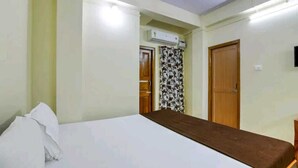 Una habitación con una cama, una puerta de madera, un equipo de aire acondicionado y una cortina estampada.