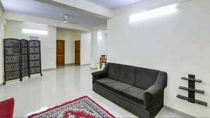 Un salón amplio con un sofá gris, un tapete estampado en rojo y blanco, un ventilador de techo y un panel decorativo negro en la pared.