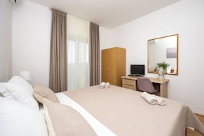 Een hotelkamer met een groot bed, een bureau met een computer, een spiegel en een raam met gordijnen.