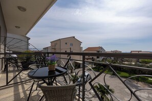 A balcony with wicker furniture, a small table with a potted plant, and a view of buildings and greenery. - Double bed Room With Private Bathroom and Balcony (Kastela)