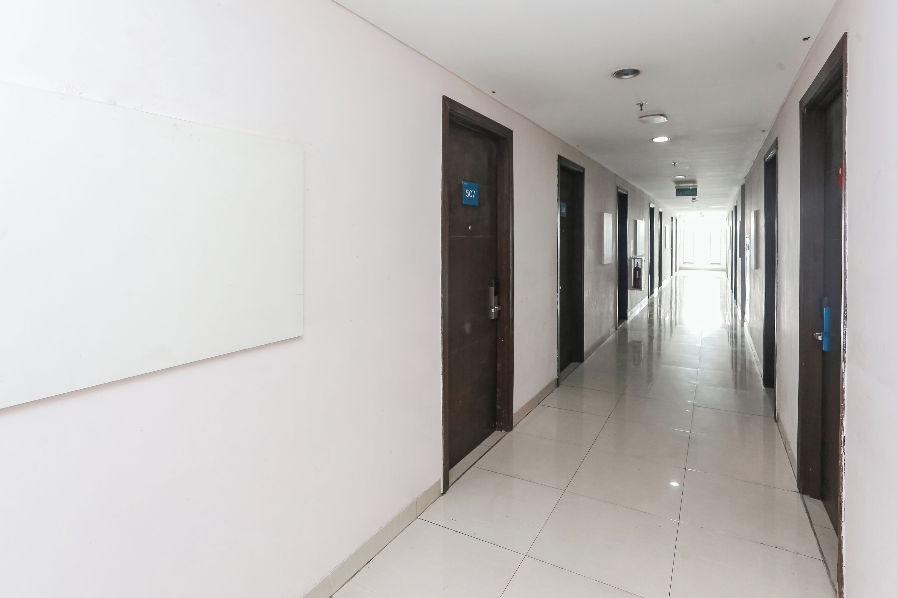 A long, narrow hallway with doors on both sides, a tiled floor, and a white ceiling with recessed lighting.