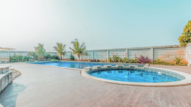 A swimming pool with a tiled edge, surrounded by a wooden deck and palm trees. - Hotel O Alfa Residence (Cikarang)
