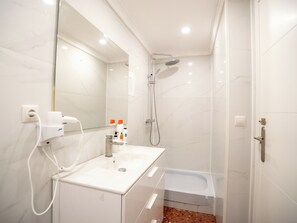 A modern bathroom with a white vanity, a shower, a bathtub, and a large mirror. - Just Hostel Capsules (Alicante)