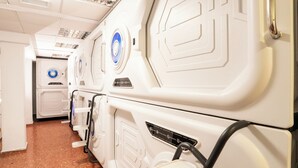 Una fila de baños de avión blancos con pomos circulares azules, techo azulejado con ventilación y suelo marrón.