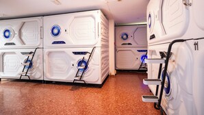 Una hilera de habitaciones de hotel blancas, de diseño moderno y compacto, con buena iluminación y un diseño uniforme, que incluyen un panel de control central y una pequeña escalera de acceso.