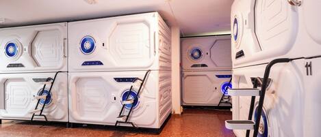 Una hilera de habitaciones de hotel blancas, de diseño moderno y compacto, con buena iluminación y un diseño uniforme, que incluyen un panel de control central y una pequeña escalera de acceso.