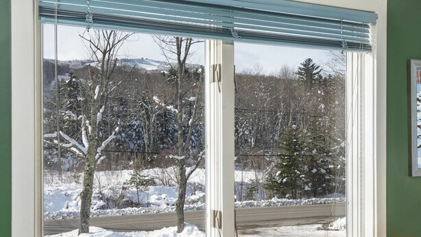 Ein Zimmer mit großem Fenster und Blick auf eine verschneite Landschaft, Holzboden und einer grünen Wand.