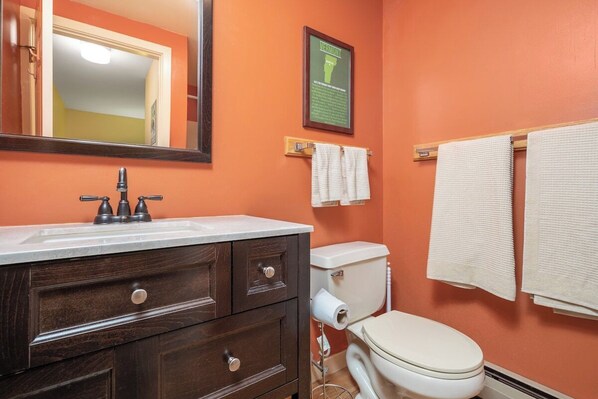 A bathroom with an orange wall, a white toilet, a wooden vanity with drawers, a mirror, and two white towels hanging on a rack.