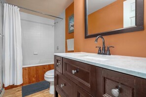 Un baño con ducha, inodoro, tocador con lavamanos y espejo.
