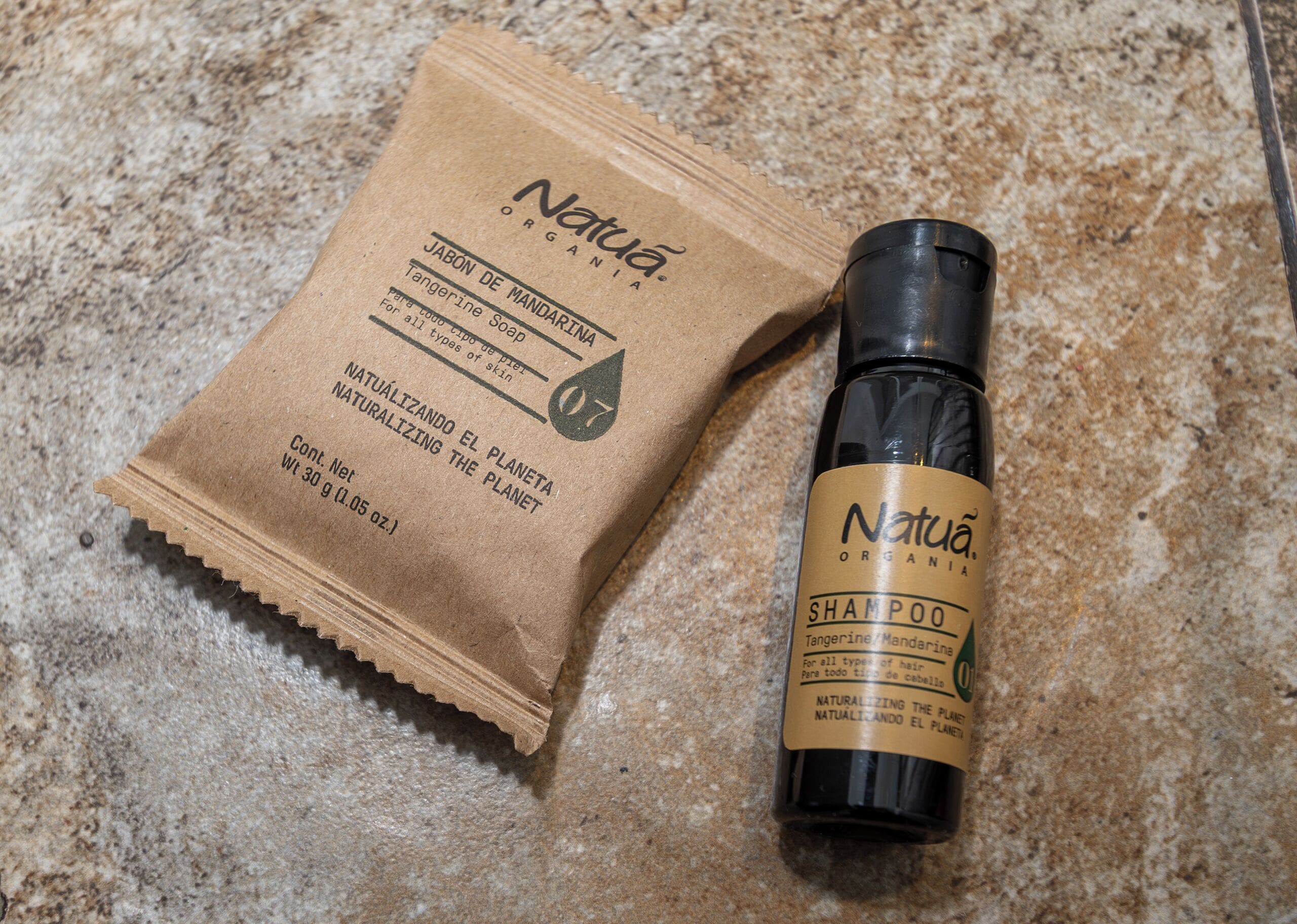 A brown paper bag and a bottle of Natuà shampoo on a textured surface.
