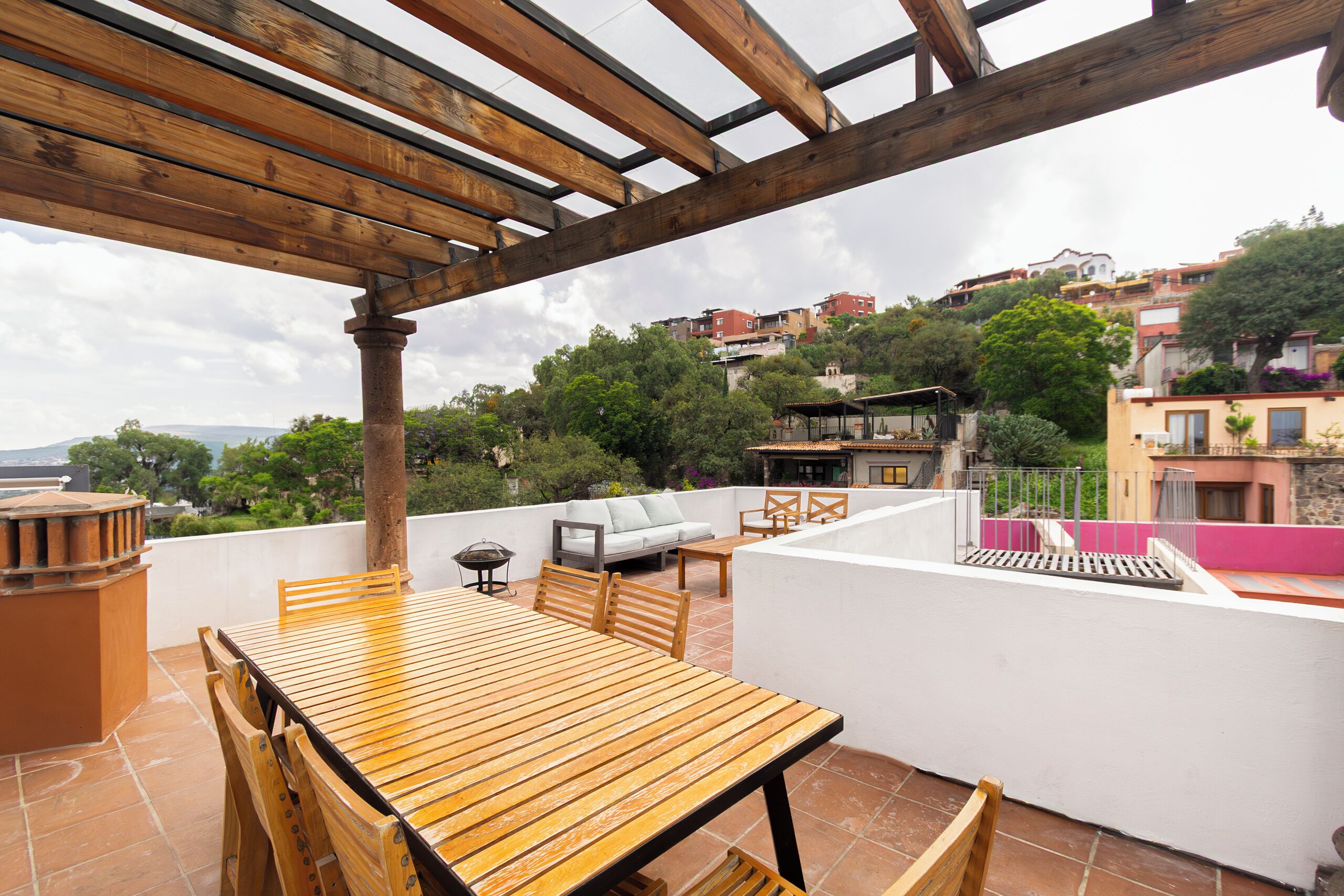 Una mesa y sillas de madera en una terraza con vistas a un pueblo en la ladera.
