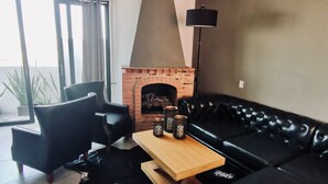 Una sala de estar moderna con un sofá de cuero negro, una mesa de centro de madera y una chimenea de ladrillo.