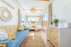 A modern bedroom with a bed, a blue sofa, a wooden cabinet, and a large window.