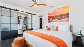 Habitación de hotel moderna con una cama grande, ventilador de techo, armario corredero y una pintura de paisaje desértico.