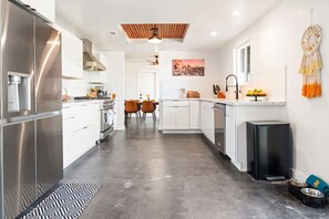 A modern kitchen with stainless steel appliances, a dining area with chairs, and a black trash bin. - Desert Heart | Stargazing Dome | Pool | Spa (Joshua Tree)
