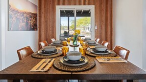Comedor con una larga mesa dispuesta para una comida, paredes de paneles de madera y un gran ventanal con vistas a la vegetación.