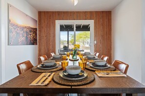 A dining room with a long table set for a meal, wooden panel walls, and a large window with a view of greenery. - Desert Heart. Stargazing Dome, Spa, Joshua Tree. (Joshua Tree)
