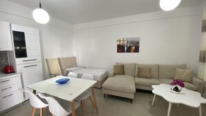 A modern, well-lit living room with a dining area, a sofa, and a small table with a vase of flowers. - Aquamarine Apartments 2, VLORE (Vlorë)