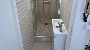 A narrow shower stall with a glass door, a handheld showerhead, and a wall-mounted faucet.