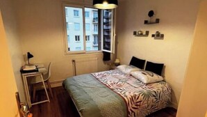 A small bedroom with a bed, a desk, a chair, a window, and a radiator.