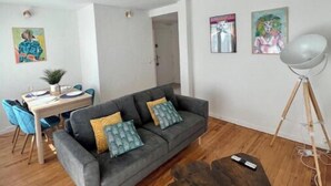 A modern living room with a grey sofa, wooden coffee table, and a dining area with blue chairs and a small table.