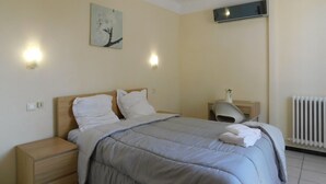 Ein Schlafzimmer mit Bett, Nachttischen, einem Nachtschränkchen, einer Heizung und einer Wand-Klimaanlage.