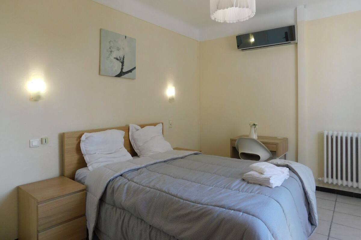 Un dormitorio con cama, mesitas de noche, un radiador y aire acondicionado instalado en la pared.