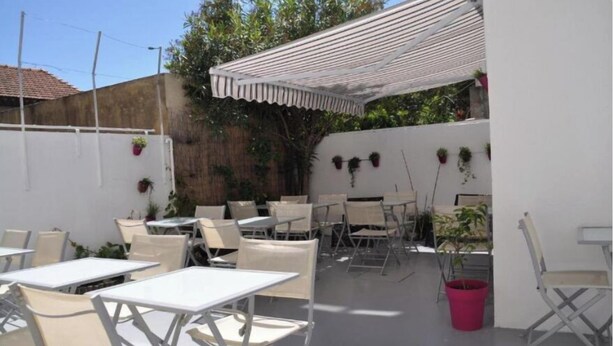 Eine Terrasse im Freien mit weißen Tischen und Stühlen, einer weißen Pergola und Topfpflanzen.