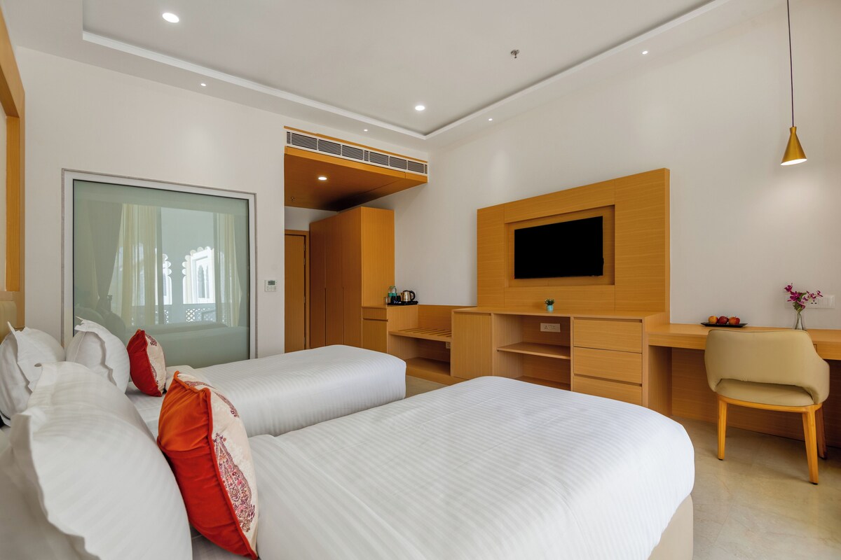 A modern hotel room with a large bed, a desk, a chair, a television, and a wardrobe.