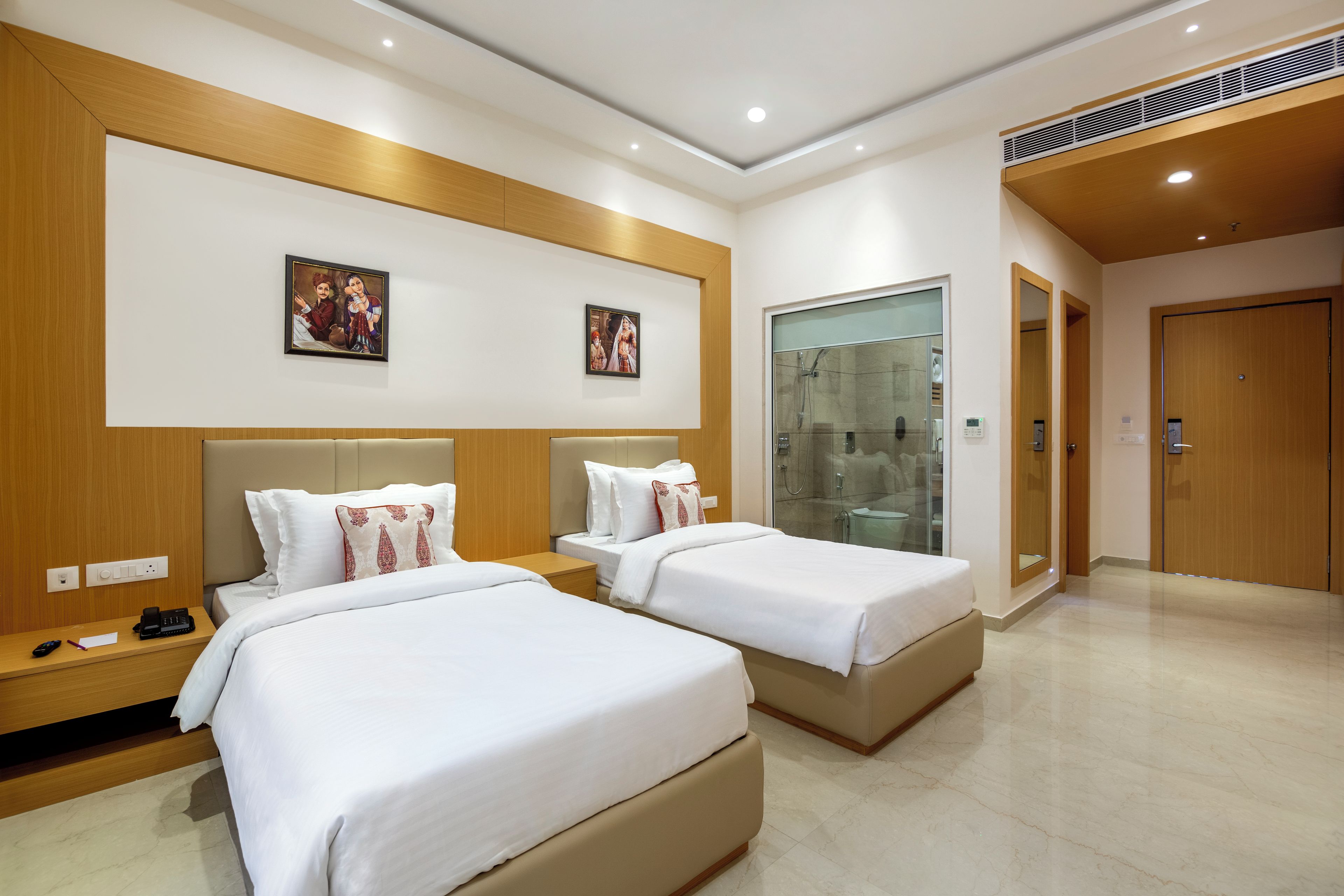 Une chambre d’hôtel avec deux lits, une douche, une tête de lit en bois et un téléphone fixé au mur.