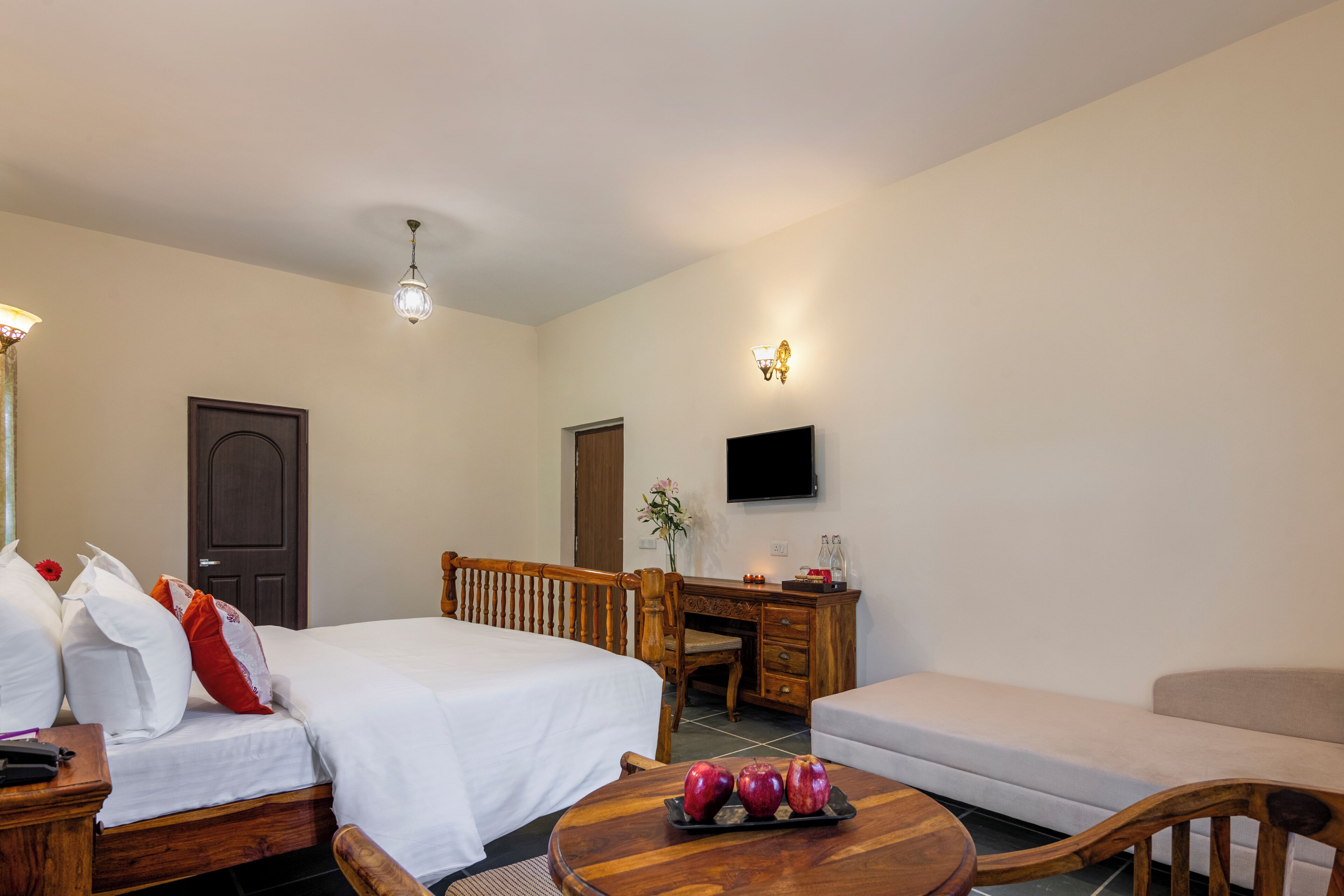 A hotel room with a bed, a desk, a chair, a sofa, and a round wooden table with apples.