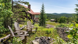 Une cabane dotée d’une véranda, entourée de verdure et offrant une vue sur les montagnes.