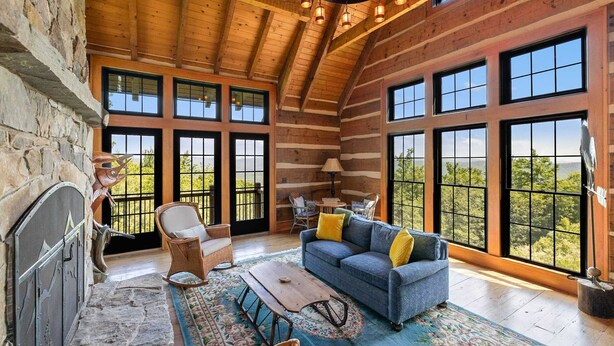 A spacious living room with a stone fireplace, large windows, and a high wooden ceiling. - Mountainside 5-BR Ski-In/Out Okemo Villa (Ludlow)