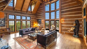A spacious log cabin interior with large windows, a fireplace, and a rustic bear statue. - Mountainside 5-BR Ski-In/Out Okemo Villa (Ludlow)