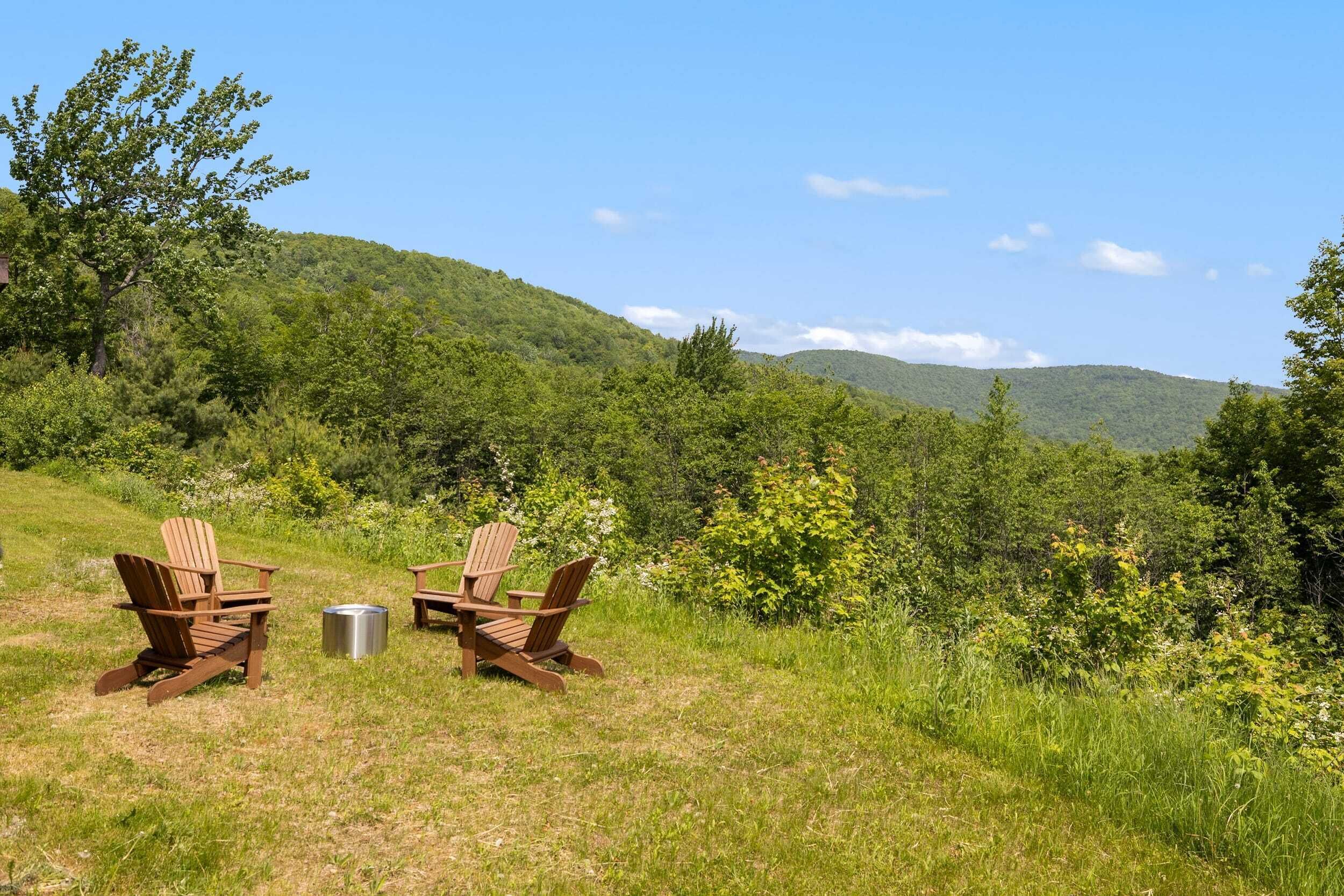 Due poltrone Adirondack e un cestino metallico in una zona erbosa con vista su una collina boscosa.