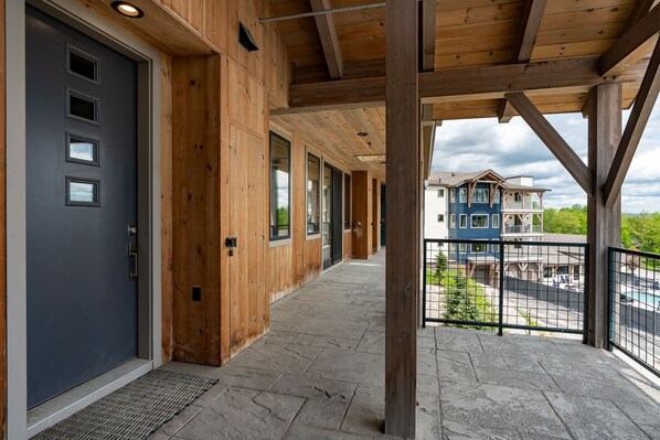 A covered outdoor area with wooden beams, a stone floor, and a view of a house in the background. - Ski-In/Out Condo on Okemo Mountain (Windsor County)