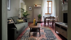A living room with a sofa, a coffee table, a dining table with chairs, a TV, and a patterned rug. - Pergola One Romantic Apt by Oteego (Florence)