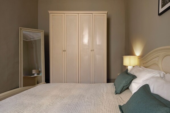 A bedroom with a bed, a nightstand with a lamp, a wardrobe, and a mirror.
